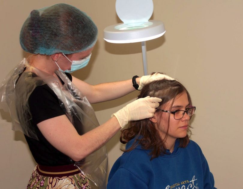 An assistant in the clinical head lice trial treats a participant in the study at the University of Canberra
