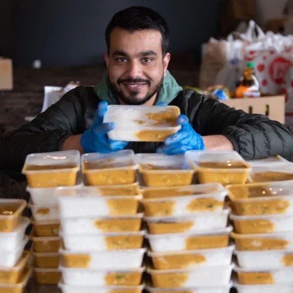 A smiling man holding two takeaway boxes full of food