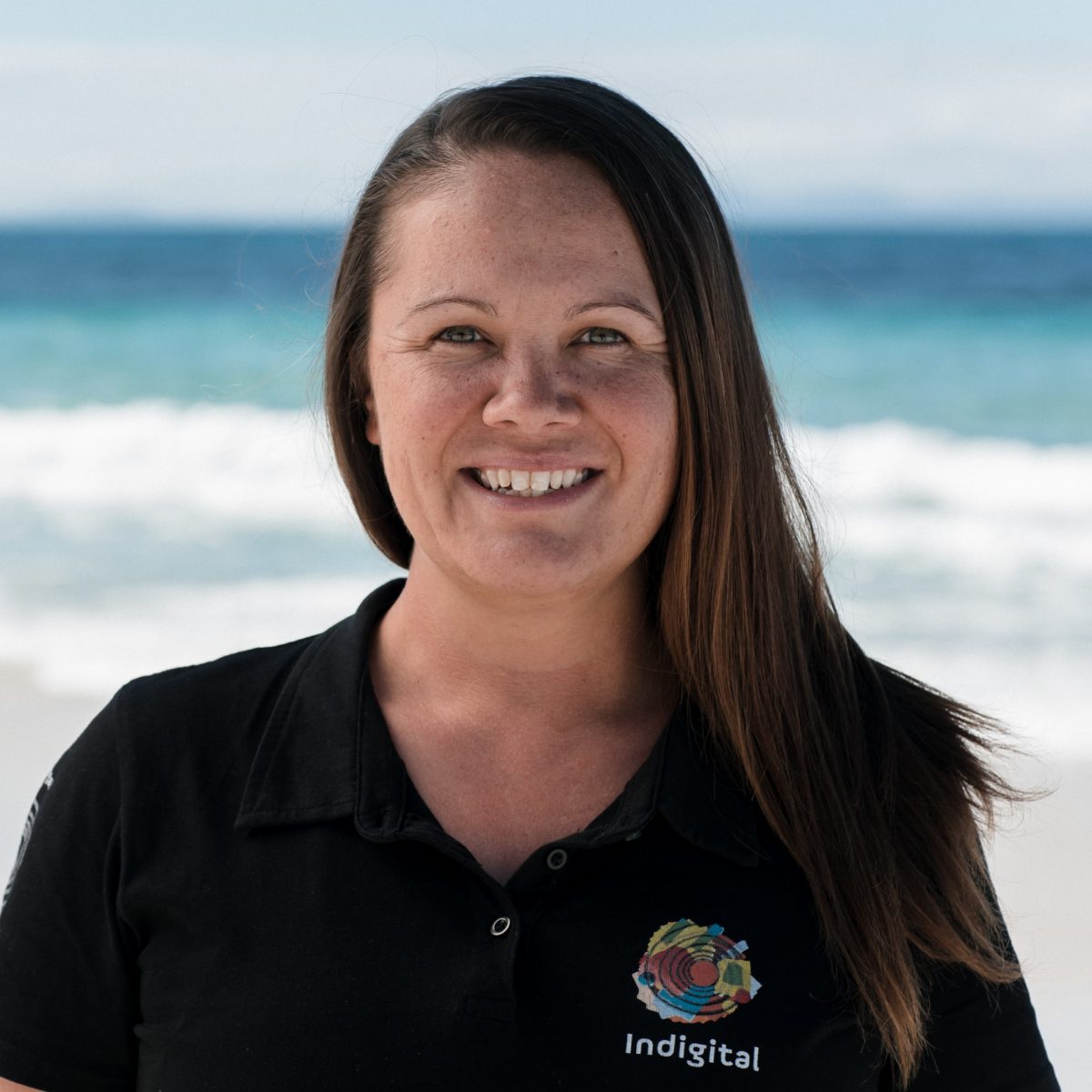 A smiling woman in a black polo shirt in front of the ocean
