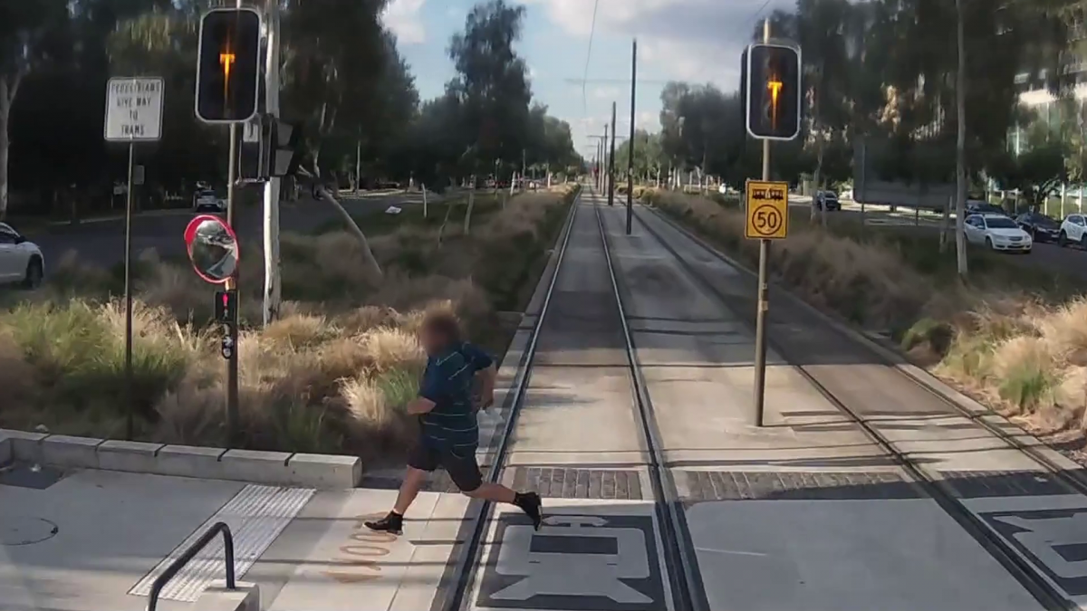A man is pictured running across a light rail track in Canberra from the train driver's point of view, causing the train driver to suddenly brake