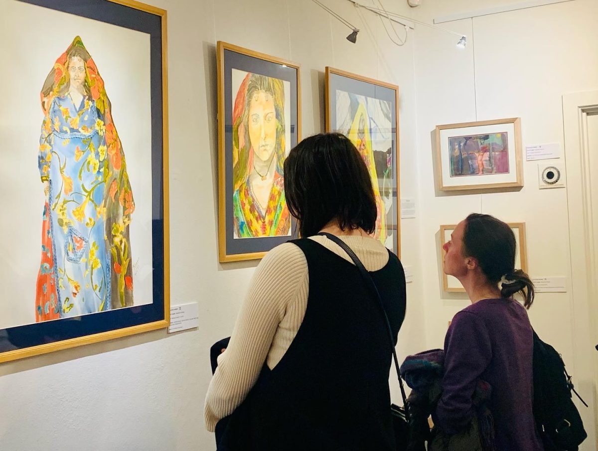 Two women in an art gallery looking at framed artworks