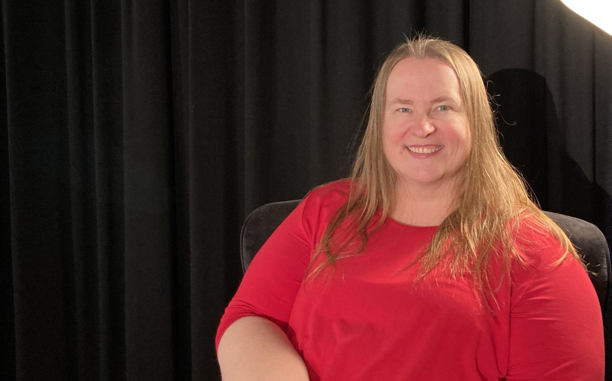 A woman with her blonde hair loose wearing in a red shirt sitting down