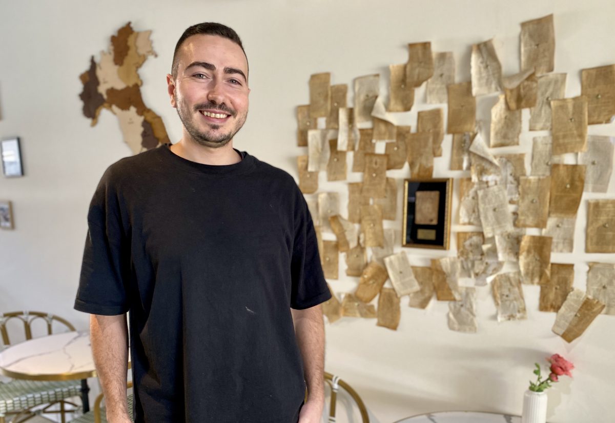 Man wearing black t-shirt stands in front of wall decorated with pages of a book.