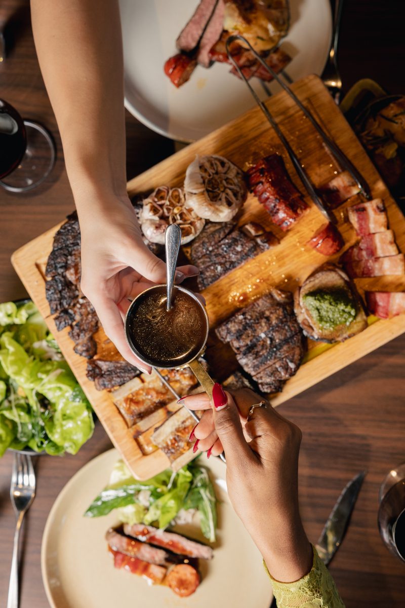 a hand passing a cup of sauce to another hand across a table of food